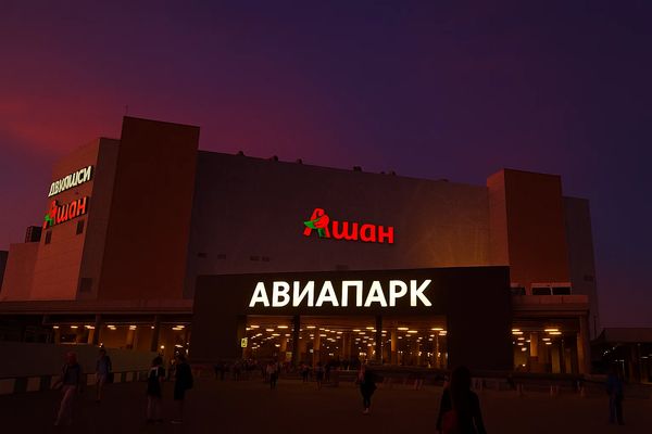 Фасад торгово-развлекательного центра «Авиапарк» в Москве вечером, видна вывеска на фоне темного неба, посетители входят в здание