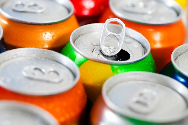 Открытая алюминиевая банка с газированным напитком среди других разноцветных банок, символизирующая рынок безалкогольных напитков летом