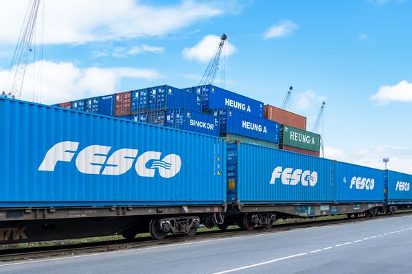 Контейнерный поезд FESCO с экспортным грузом на фоне портовых кранов и штабелей контейнеров в морском терминале