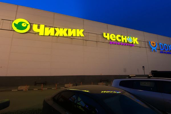 Вывески дискаунтеров «Чижик» и «Чеснок» на фасаде торгового центра вечером — лидеры роста среди FMCG-ритейлеров в России в 2024 году
