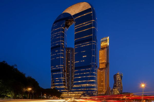 Современный небоскрёб One в Москва-Сити в вечернее время с архитектурой в виде ленты Мёбиуса, освещённый фасад и окружающие деловые здания