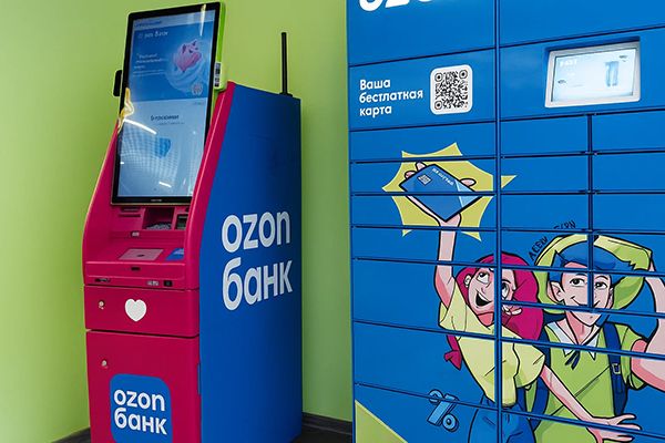 Банкомат Ozon-банка рядом с постаматом в фирменном дизайне внутри пункта выдачи заказов маркетплейса.