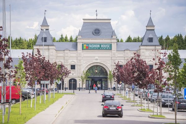 Главный вход в аутлет Fashion House Group в Шереметьево с парковкой и посетителями на фоне зелёного леса
