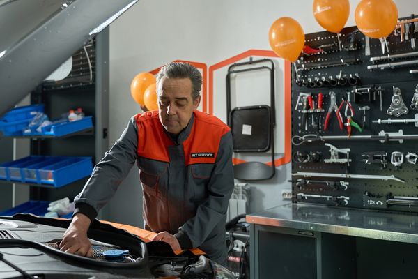 Механик FIT SERVICE выполняет диагностику двигателя автомобиля в современной мастерской с инструментами и брендированным оформлением
