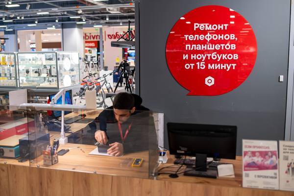 Сервисная зона М.Мастер в магазине М.Видео: специалист производит ремонт смартфона за стойкой с табличкой «ремонт от 15 минут»