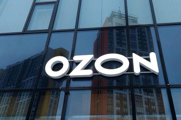 Логотип Ozon на фасаде офисного здания с отражением городских высоток в стеклянных окнах