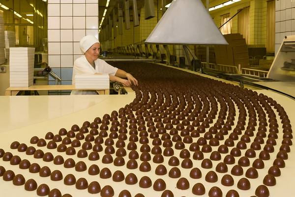 Производственная линия на кондитерской фабрике: выпуск шоколадных конфет, сотрудница контролирует качество — иллюстрация темы подорожания шоколада и цепочек поставок