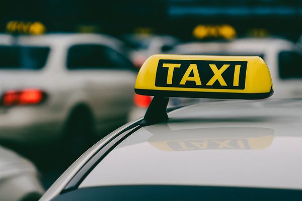 Желтая таксомоторная табличка на крыше автомобиля на фоне городского трафика — символ рынка такси
