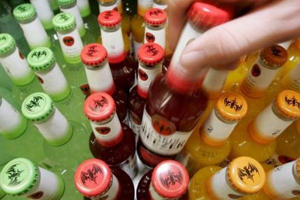 Рука покупателя берет бутылку слабоалкогольного коктейля среди ассортимента разноцветных напитков в холодильнике магазина.