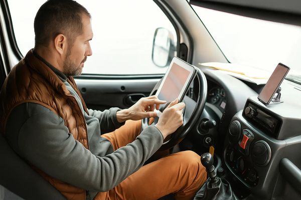 Водитель грузового автомобиля оформляет электронный перевозочный документ на планшете в салоне машины