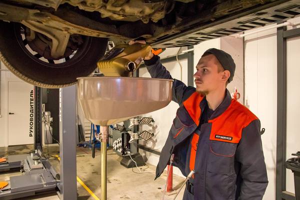 Механик заливает моторное масло в автомобиле на станции техобслуживания FIT SERVICE
