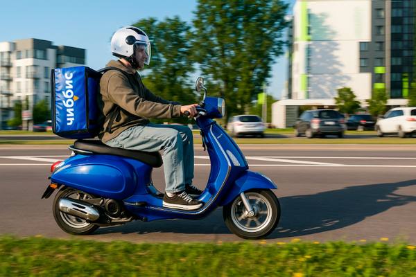 Курьер сервиса доставки еды «Чиббис» на синем скутере в движении по городу, дневная съемка