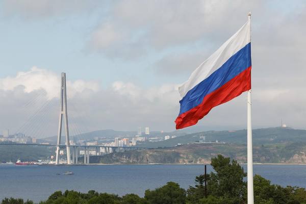 Флаг России на фоне бухты Золотой Рог и моста на остров Русский во Владивостоке — символ развития логистики и партнерств на Дальнем Востоке