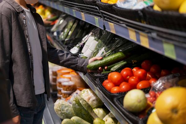 Покупатель выбирает свежие овощи на полке продуктового магазина у дома — томаты, огурцы, авокадо и салат в зоне самообслуживания