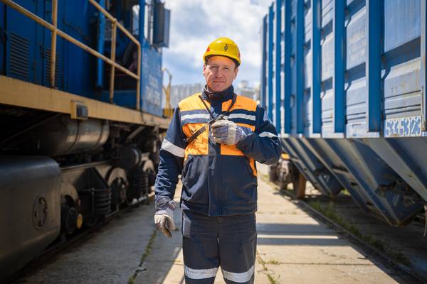 Сотрудник Туапсинского балкерного терминала в форме и каске на фоне вагонов с минеральными удобрениями и локомотива на ж/д путях