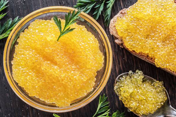 Стеклянная миска с белой икрой и бутербродом на чёрном столе, крупный план зёрен икры, иллюстрация роста спроса на белую икру и её перехода в категорию повседневных продуктов