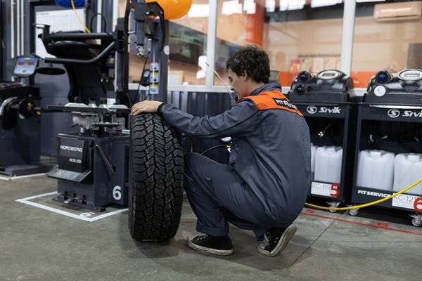 Сотрудник автосервиса проверяет зимнюю шину перед установкой на балансировочном станке
