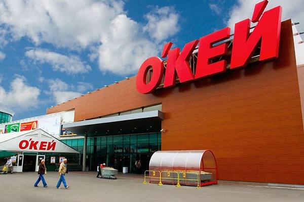 Фасад гипермаркета «О’Кей» с крупной красной вывеской и входом для покупателей на фоне голубого неба, иллюстрация сделки по передаче сети под управление менеджмента