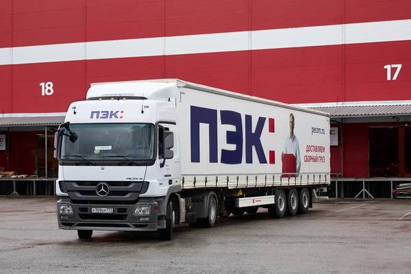 Грузовик логистической компании ПЭК на фоне красного фасада логистического центра