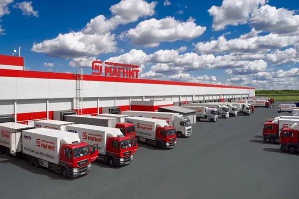 Распределительный центр сети «Магнит» с рядом брендированных грузовиков у погрузочных ворот, логистический хаб для снабжения магазинов в регионе
