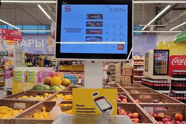 Интеллектуальные весы с сенсорным экраном и камерой в супермаркете «Магнит», демонстрирующие интерфейс распознавания товаров на фоне фруктово-овощного отдела