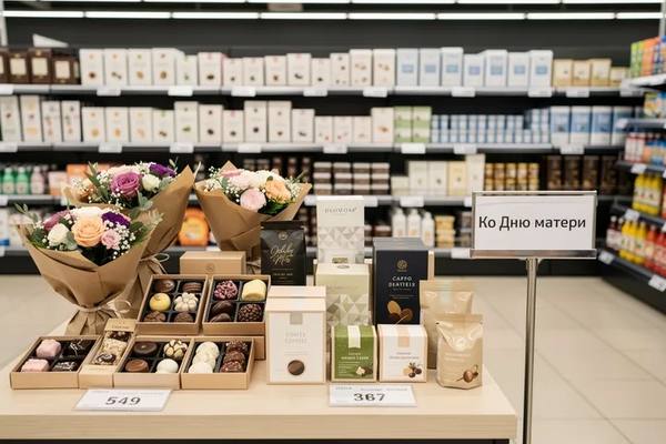 Подарочная выкладка в супермаркете с цветами, сладостями и наборами к Дню матери, иллюстрирующая покупательские предпочтения россиян