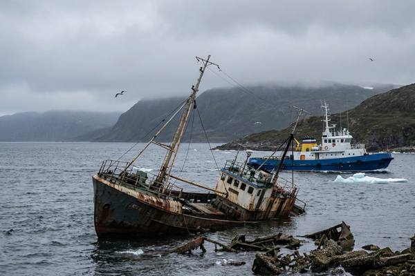 Старое ржавое судно, выброшенное на берег в российском порту, на фоне рабочего буксира — визуализация обновления флота и последствий запрета на устаревшие суда
