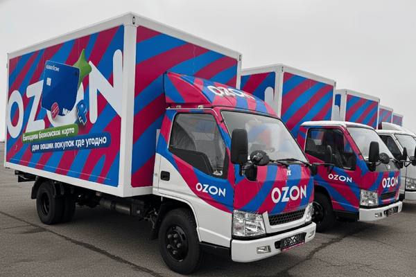 Ряд брендированных фургонов Ozon AMBERTRUCK JL на парковке, курьерские грузовики маркетплейса для доставки заказов в пункты выдачи и малые города