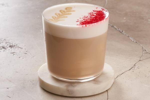 Стакан латте с плотной молочной пеной и красной ягодной посыпкой на мраморной подставке, сезонный напиток кафе «Перекрёсток Select»