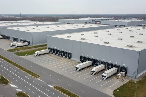 Современный логистический парк в России: склады класса A и грузовики у погрузочных доков, иллюстрация перехода от built-to-suit к аренде.