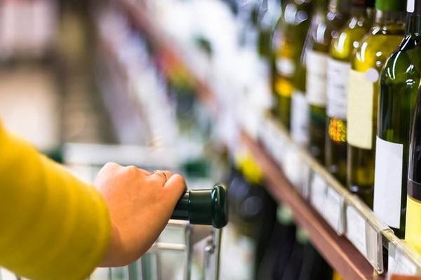 Покупатель с тележкой выбирает вино в супермаркете — крупный план бутылок на полке и руки в фокусе