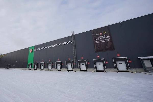 Фасад распределительного центра X5 Group в Кемерово с зонами разгрузки и логотипами торговых сетей «Пятёрочка» и «Чижик» на фоне зимнего пейзажа