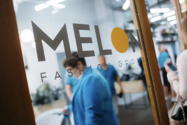 Логотип Melon Fashion Group на стекле офисного помещения, сотрудники компании на фоне