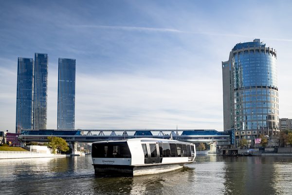 Электрическое речное судно на Москве-реке на фоне современных деловых зданий; иллюстрация развития экологичного городского транспорта.