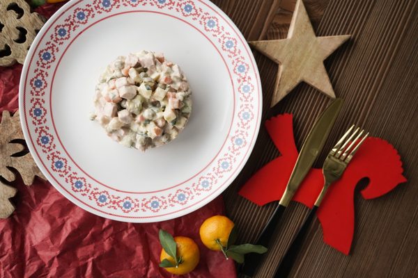 Традиционный салат Оливье на праздничном столе с новогодним декором и мандаринами