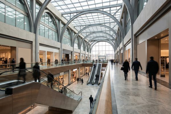 Интерьер современного торгового центра с просторным атриумом, витринами и потоками посетителей; иллюстрация роста объёмов строительства и рекордного ввода торговых площадей.