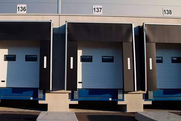 Погрузочно-разгрузочные доки современного складского комплекса с нумерованными воротами, элементами док-левеллеров и уплотнителями для приёма грузового транспорта