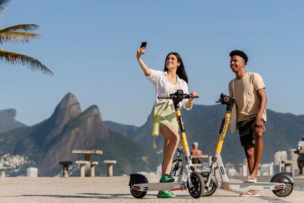 Пользователи на электросамокатах Whoosh на фоне прибрежного города в Латинской Америке, иллюстрирующие выход сервиса на рынок Колумбии и рост микромобильности