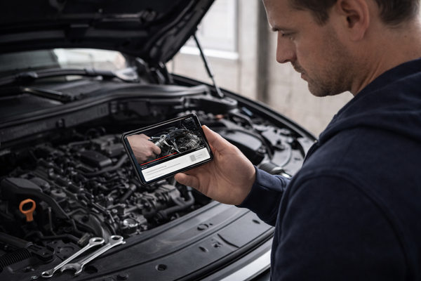 Автовладелец смотрит видеоинструкцию по ремонту на смартфоне у открытого капота автомобиля — риск неправильных советов