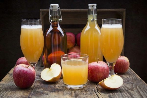 Бутылки и бокалы натурального яблочного сидра с яблоками на деревянном столе — иллюстрация к статье о росте производства сидра и дефиците технического яблока в России