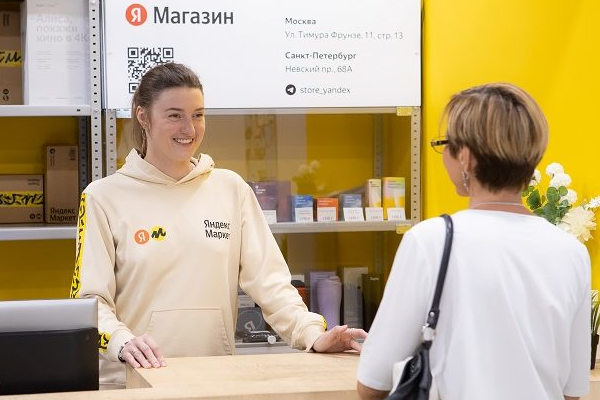 Сотрудник пункта выдачи Яндекс Маркета общается с клиентом у стойки, демонстрируя важность сервиса и атмосферы в ПВЗ