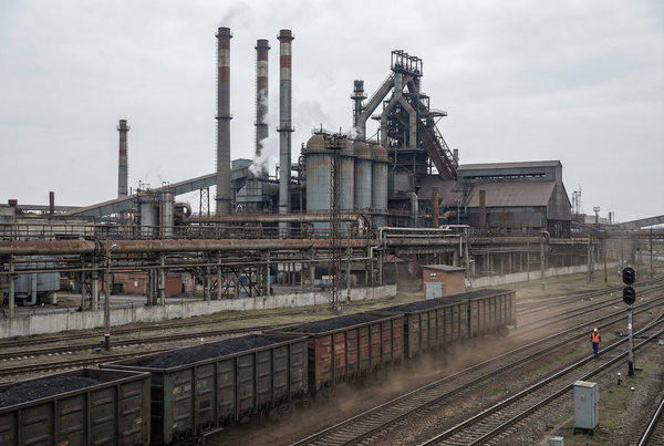 грузовой железнодорожный состав проходит мимо промышленного предприятия — давление на сырьевые отрасли и транспортную логистику в России