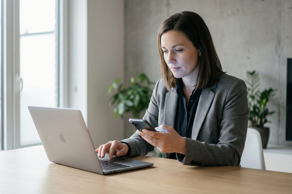 деловой пользователь работает с ноутбуком и смартфоном, подтверждение электронной подписи онлайн через мобильное приложение