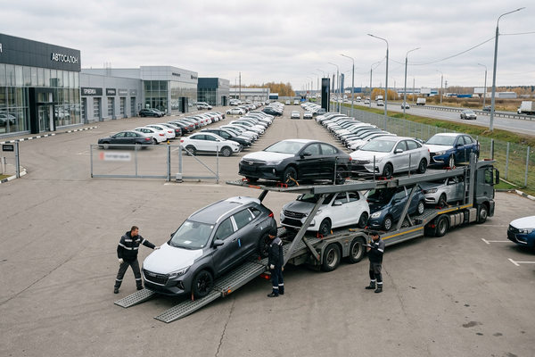 Разгрузка автовоза с новыми легковыми автомобилями на площадке дилерского центра — логистика поставок и распределение автомобилей на российском рынке