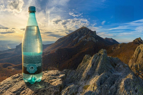 бутылка минеральной воды Новотерская на фоне гор Кавказа, производство и источники минеральной воды в России
