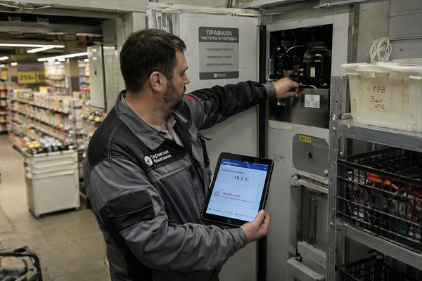 Инженер проверяет холодильное оборудование в супермаркете с планшетом диагностики, автоматизация мониторинга и ремонта в ритейле