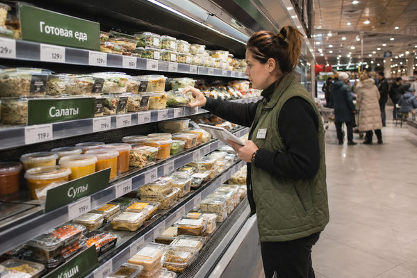 Сотрудник продуктового магазина проверяет витрину с готовой едой, салатами и супами в упаковке