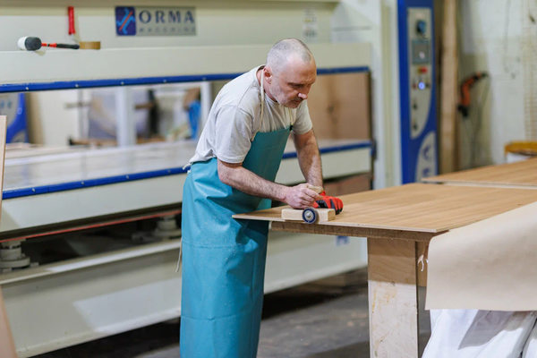 Сотрудник мебельного производства обрабатывает деревянную панель в производственном цехе