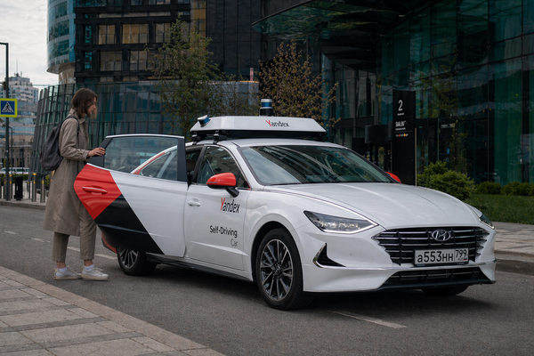 Беспилотный автомобиль Яндекса у тротуара в деловом районе: пассажир садится в роботакси в городской среде