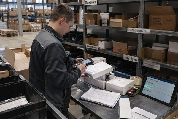 Сотрудник склада маркетплейса сканирует коробки с электроникой перед приемкой, технологический сбор на смартфоны и ноутбуки